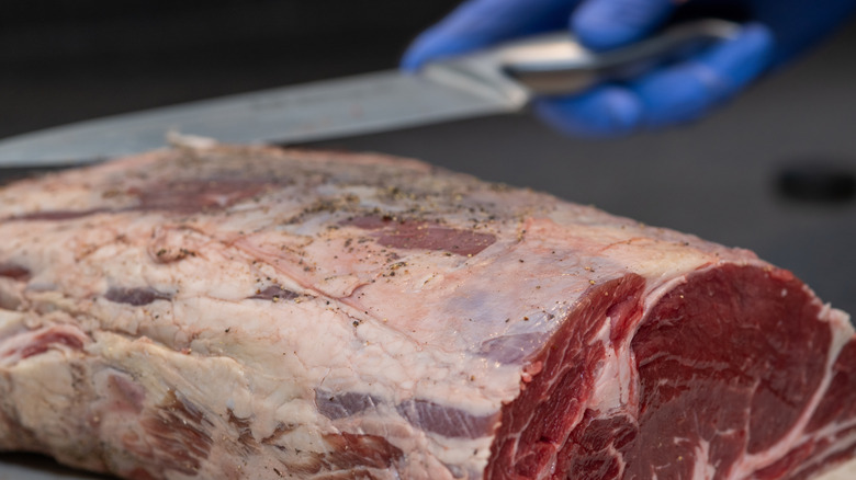 A butcher trims fat from a prime rib roast