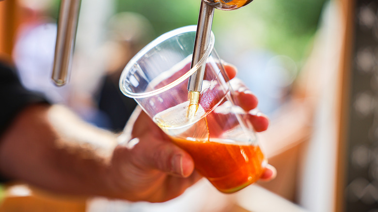 person filling a plastic cup with beer from the tap