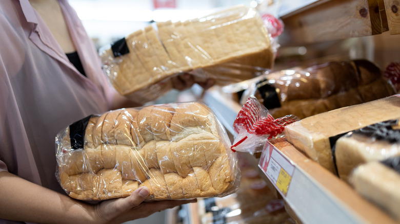 Woman holding two sliced, packaged loaves of bread in a store