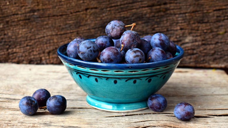 A bowl overflowing with wild plums on a wooden table.