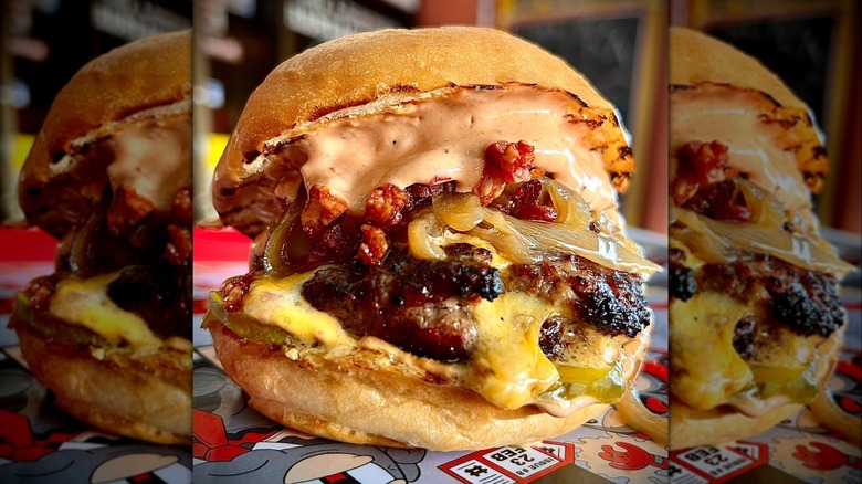 Large, loaded burger from High N' Dry with drippy sauce, onions, pickles, and bacon bits