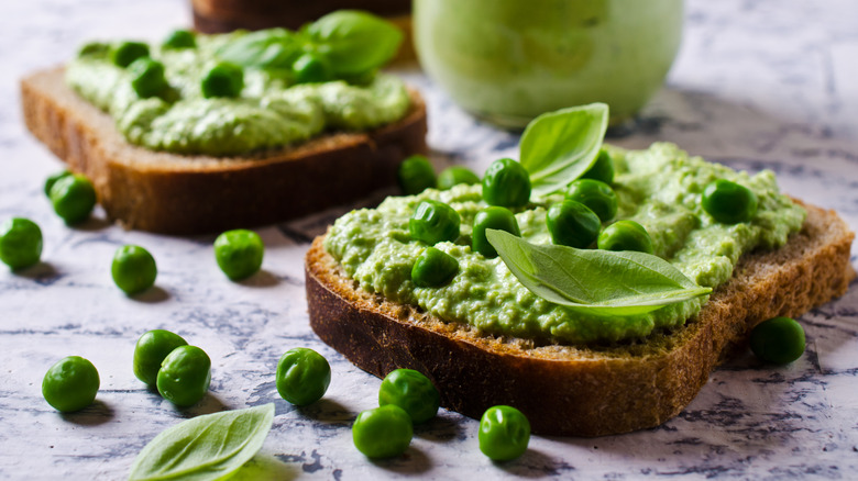 Two slices of bread topped with smashed peas, whole peas, and basil garnish.