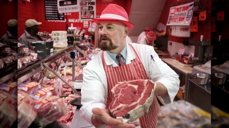 Butcher in red hat displays large cut of beef