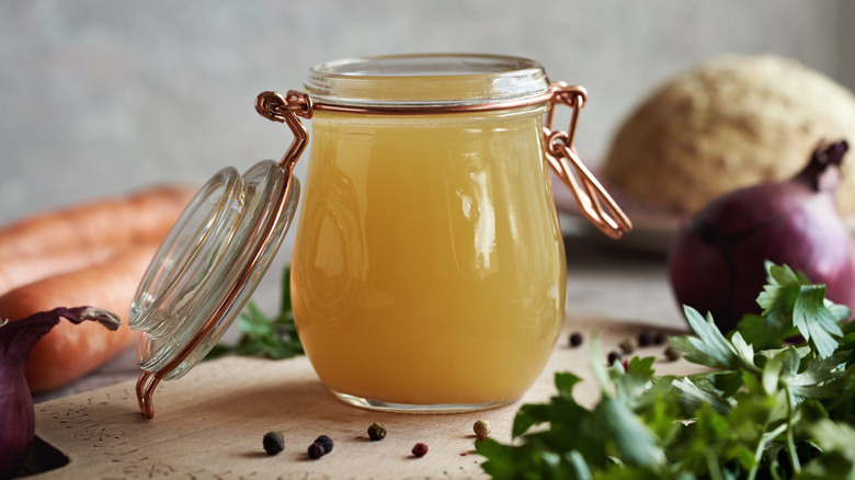 Glass jar with hinge lid open of chicken stock surrounded by aromatics