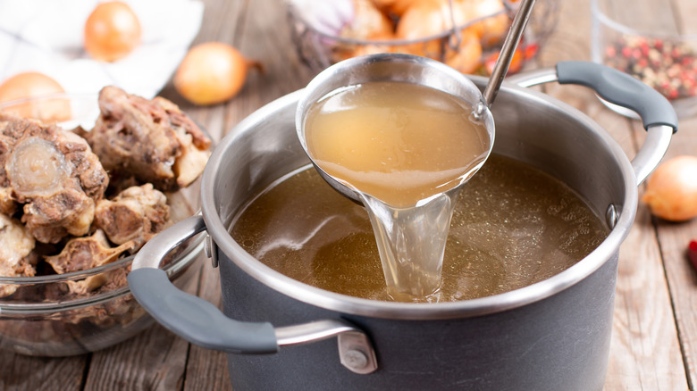 Ladle pouring lifting strained stock out of a pot, beef bones in the background