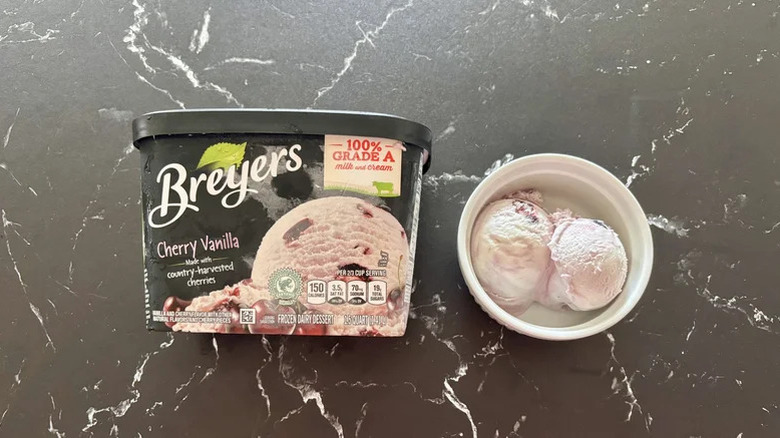 Container of Breyers Cherry Vanilla next to bowl with scoops of ice cream