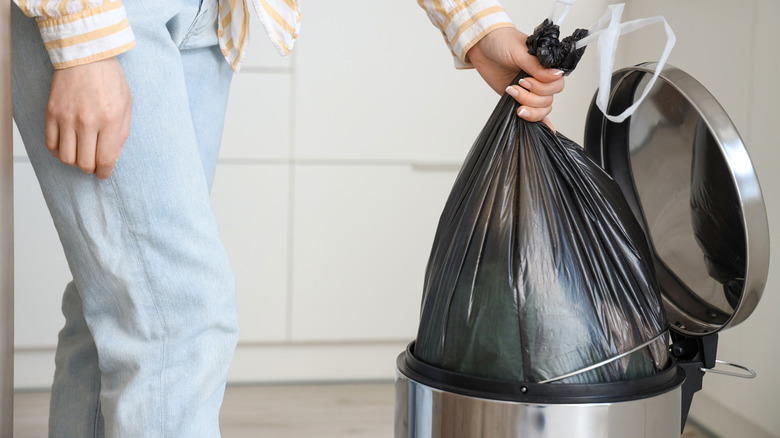 Person taking black plastic trash back out of silver garbage can
