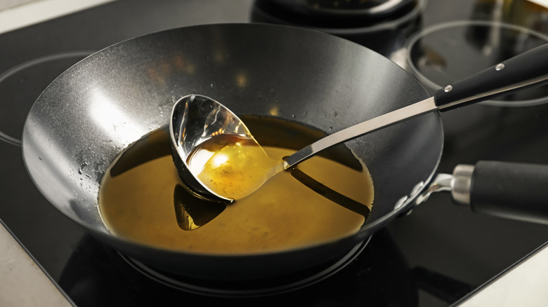 Black wok pan full of used cooking oil with steel ladle inside