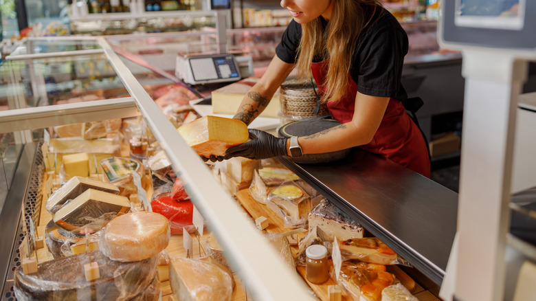 A worker picks up cheese from behind a deli counter