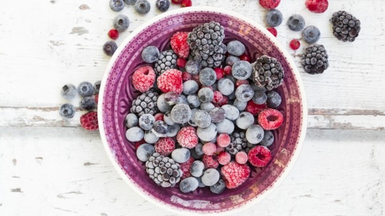 Frozen berries in a purple bowl on a white wooden surface