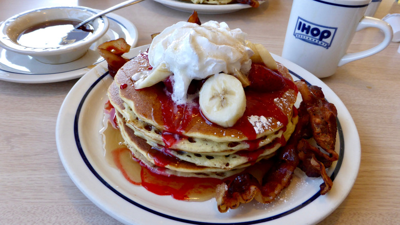 Pancake stack topped with fruit and whipped cream, with an IHOP mug in the background