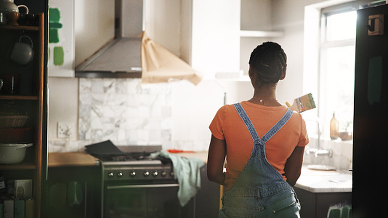 Woman stands in front of kitchen with paint brush in hand