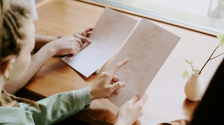 two people peruse a restaurant menu and discuss options