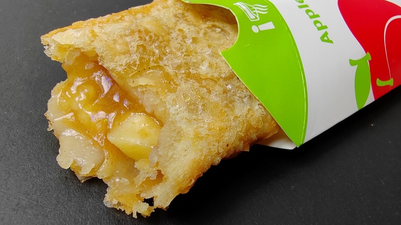 A McDonald's apple pie showing the filling and crust half inside the wrapper, with a gray background