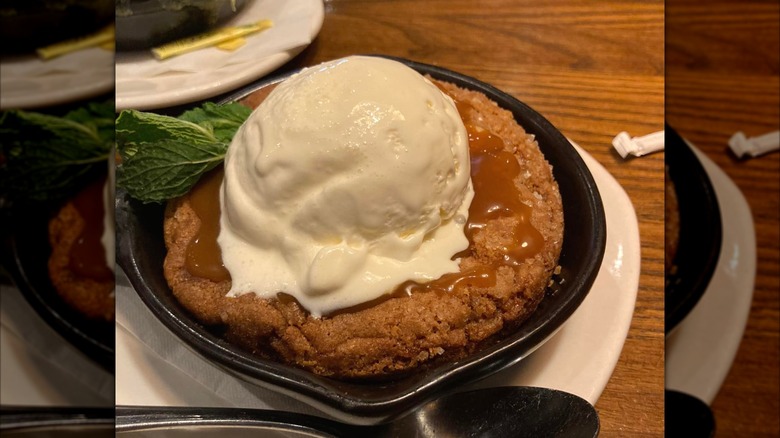 Outback Steakhouse Salted Caramel Cookie Skillet topped with ice cream and mint leaves, on a white plate on a wooden dining table