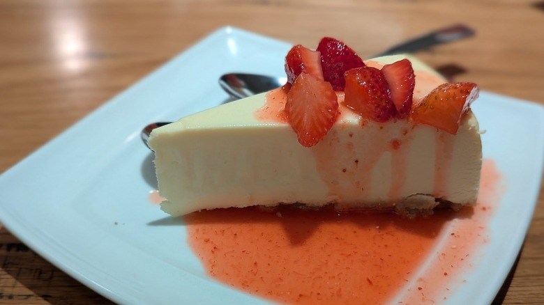 Olive Garden cheesecake with strawberry topping on a white plate on wooden table with spoons