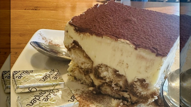 Olive Garden tiramisu on plate with spoon and mints, on wooden table with mirror borders
