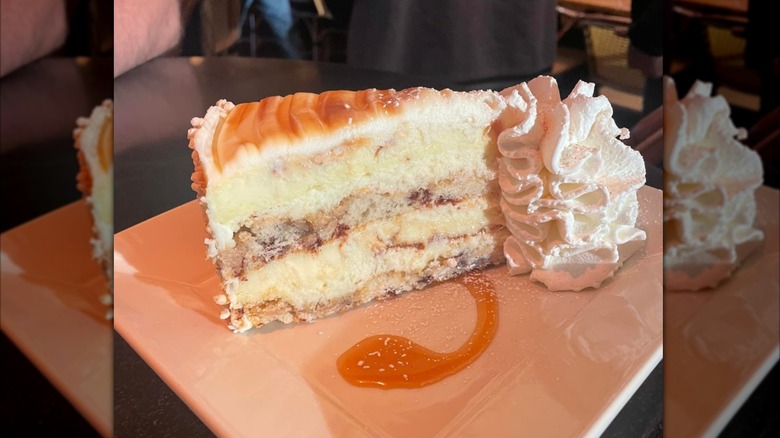 The Cheesecake Factory Cinnabon cheesecake slice with whipped cream on a white plate, on a dark dining table with mirror borders