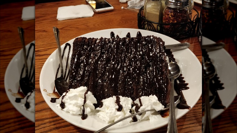 Uno towering chocolate cake on a white plate with whipped cream and spoons on a dining table
