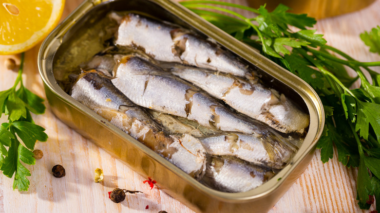 Open can of sardines on table surrounded by garnish