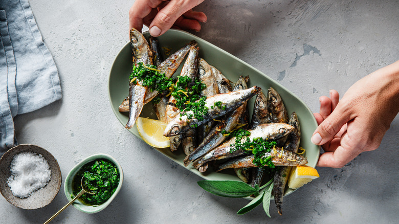 Hands serving grilled sardines with spices on a table
