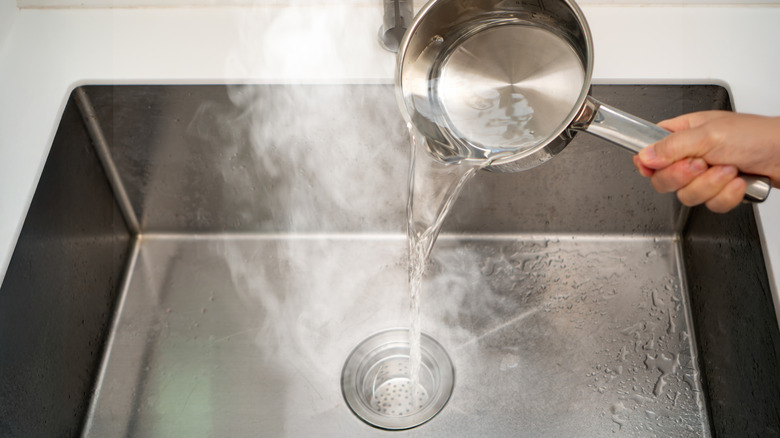 Hand pouring boiling water from a pot into the sink