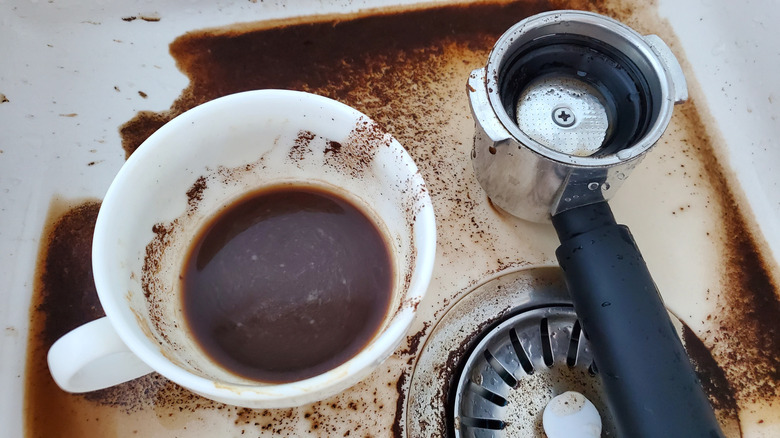 Spilled coffee in a kitchen sink alongside the mug and the portafilter