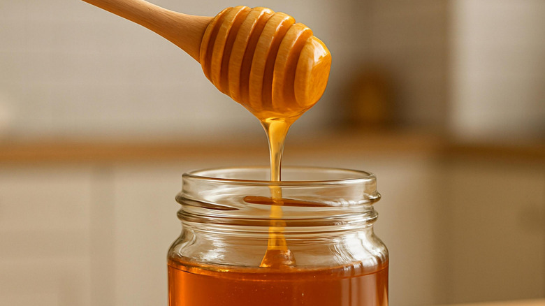 Honey dripping into the jar from a wooden honey dripper