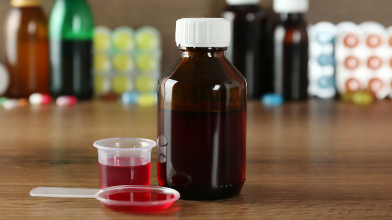 Bottle of liquid medicine in the forefront with other medicines blurred in the background