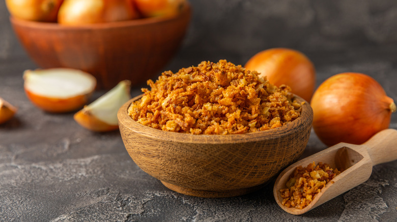 A wooden bowl of crispy fried onions next to a scoop