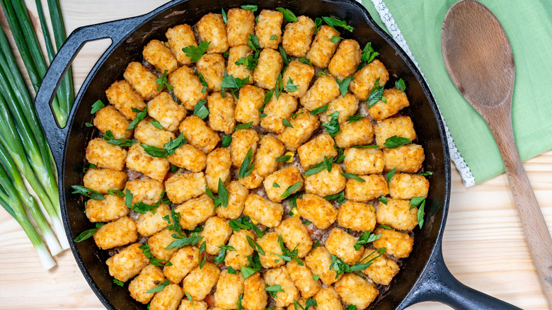 Tater tot hot dish sprinkled with parsley and green onions in a cast iron skillet