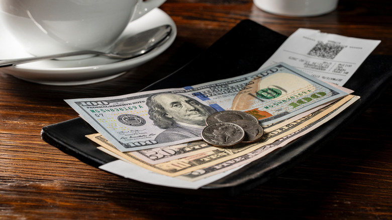 A stack of dollars and change on a restaurant receipt after eating at a restaurant