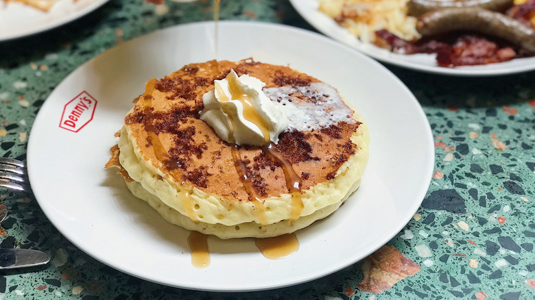 Denny's pancakes with a dollop of whipped cream drizzled with rich maple syrup
