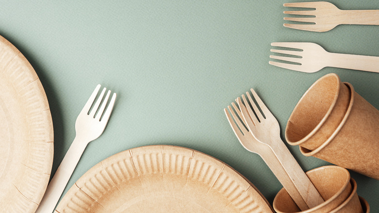 Disposable eco paper cups and wooden forks on green background flat lay view