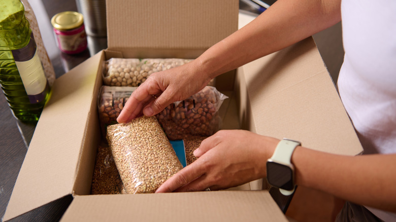 A close-up view of a person storing various food items, including grains and beans in a cardboard box