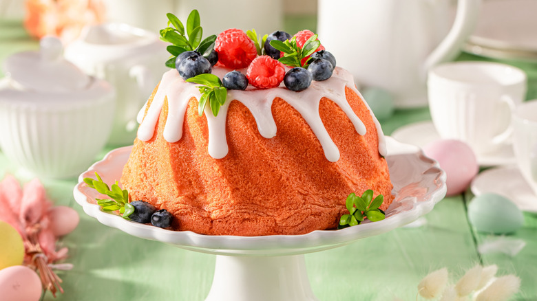 A fruit topped, glazed Bundt cake with on a cake stand