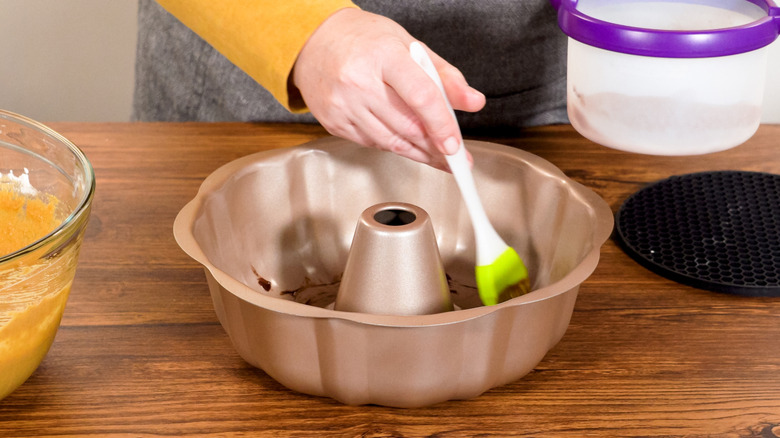 A hand brushing grease on a Bundt pan