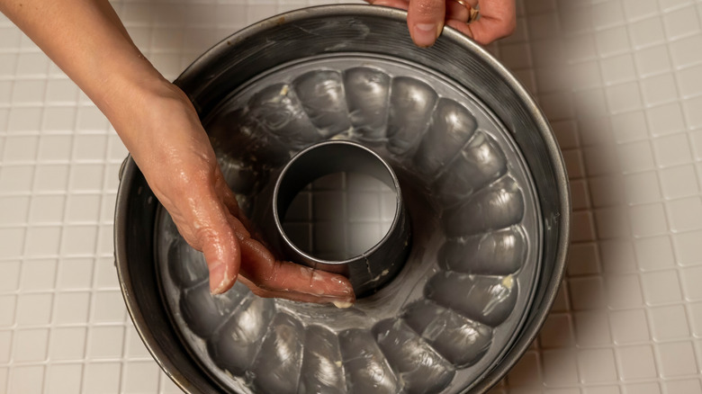 A person using their hands to grease a Bundt pan