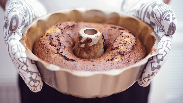 Two hands holding a baked Bundt cake in the pan