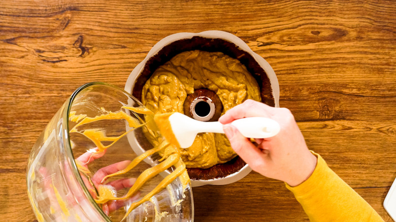 A person pouring thick cake batter into a bundt pan
