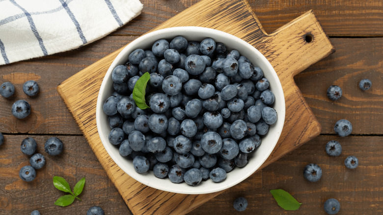 Blueberries in white bowl on wooden cutting board