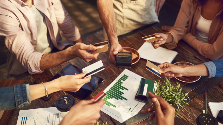 Five different people offer cards to one server holding a payment processing machine