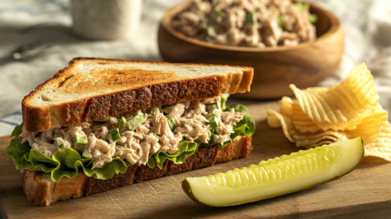 tuna salad on a sandwich with toasted bread and a pickle and chips on the side