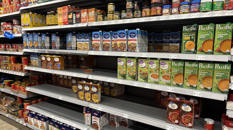 The broth and stock aisle of the grocery store with somewhat sparse shelves and a spread of different brands