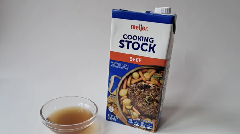 A carton of meijer beef cooking stock with a small dish of the stock alongside it on a white background