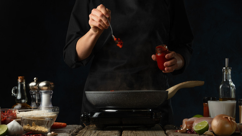 A person drops tomato paste into a pan