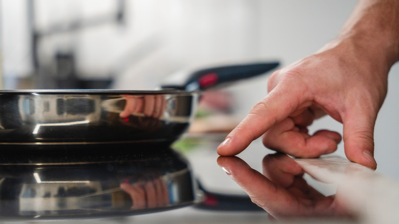 Hand turning on induction stovetop to heat a pan that's resting on top