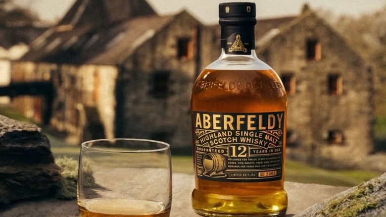 A bottle of Aberfeldy 12-year posed in front of its blurred distillery in the background