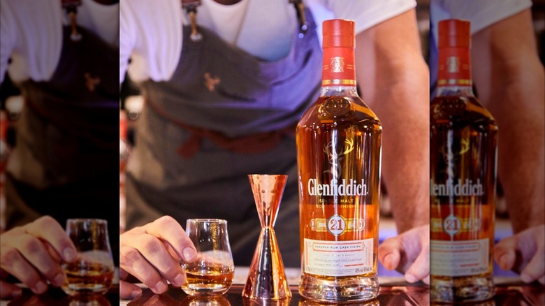 A bartender placing down a glass of whisky next to a measuring cup and bottle of Glenfiddich Gran Reserva 21-year