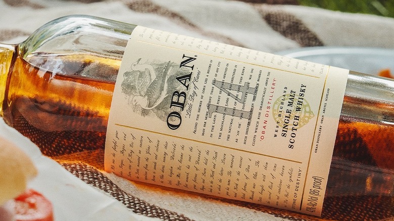 A close up of a bottle of Oban 14-year laid on its side on a picnic blanket